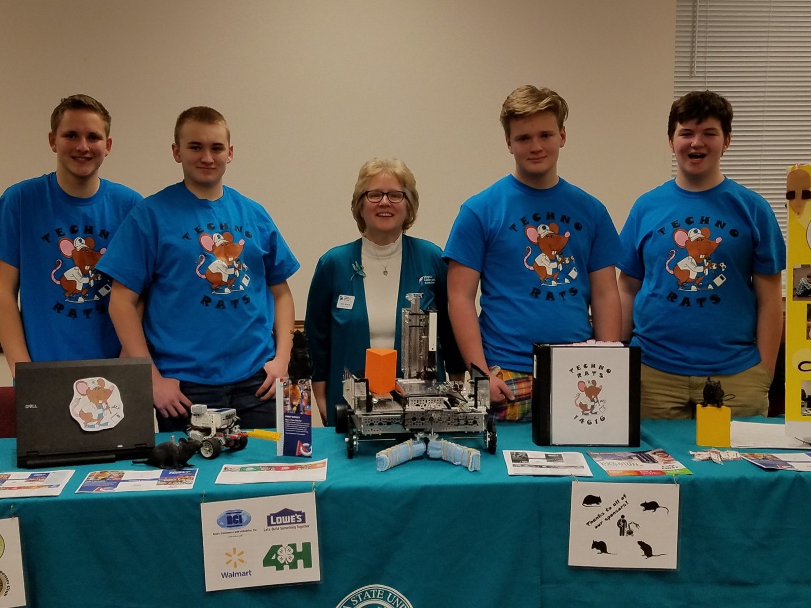 Robotics team in blue shirts with 4-H Agent and behind display table